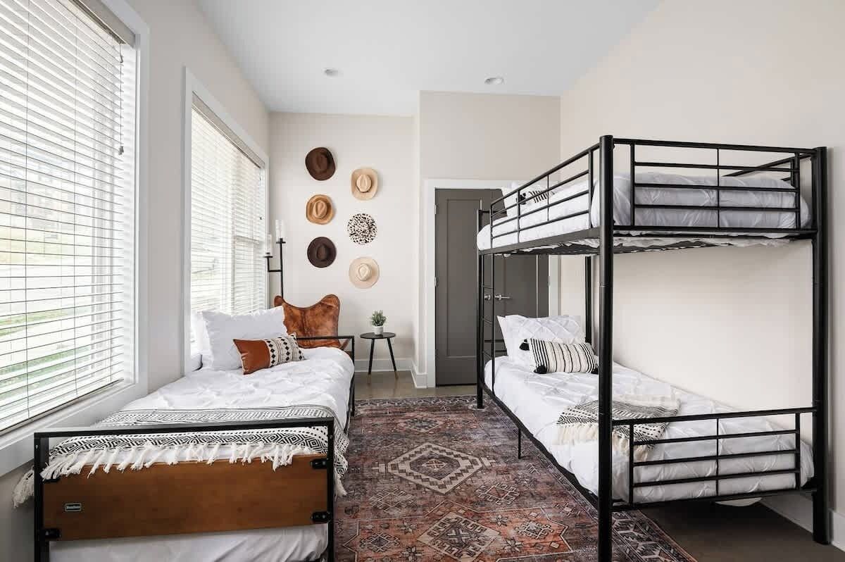 A bedroom with two bunk beds, a patterned rug, and a wall with decorative hats.