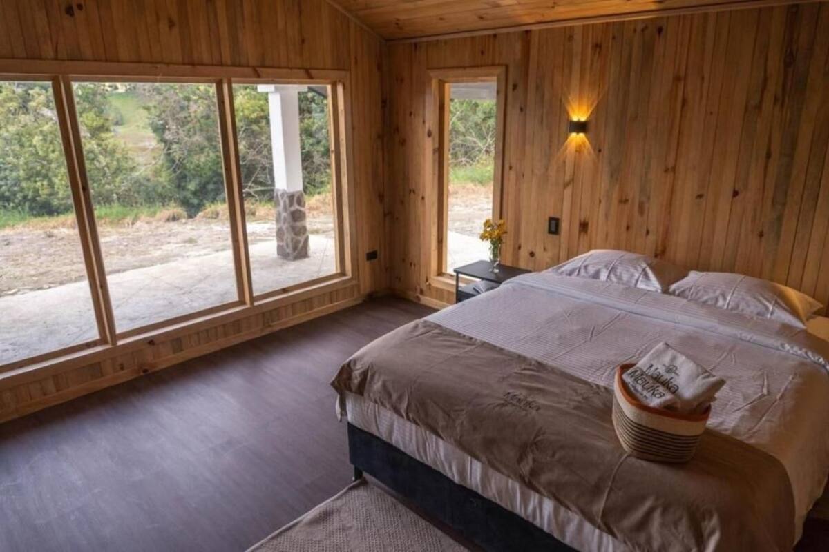 A wooden-paneled bedroom with a large bed, a nightstand, and a window with a view of the outdoors.