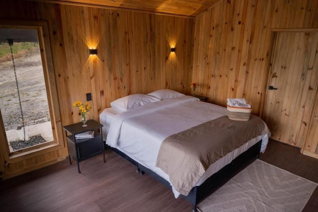 Habitación con paneles de madera, una cama, una mesita de noche y dos lámparas fijadas a la pared.