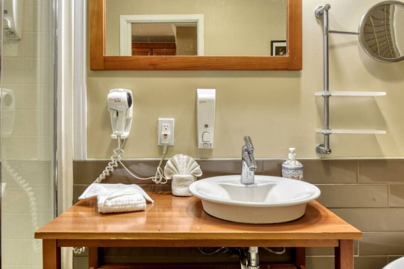 Une salle de bain avec un meuble-lavabo en bois, un lavabo blanc, un sèche-cheveux et un miroir avec un cadre en bois.