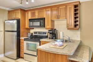 Cocina con armarios de madera, electrodomésticos de acero inoxidable, microondas, estufa y pileta.
