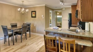 A kitchen with a dining area, wooden cabinets, a marble countertop, and a chandelier. - Condo Alpina – 3105 | Cozy Retreat in St-Sauveur (Piedmont)