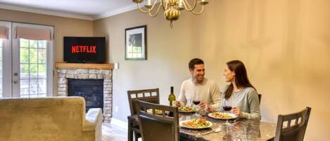 A dining area with a stone fireplace, a chandelier, and a television displaying 'NETFLIX'.