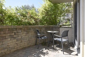 Un patio al aire libre con un muro de ladrillo, dos sillas de metal y una pequeña mesa redonda.