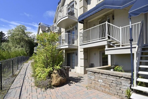 A multi-story residential building with balconies, a paved pathway, and a stone retaining wall.