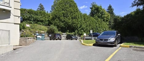 Ein Parkplatz mit Autos, ein Gebäude links und Bäume im Hintergrund.
