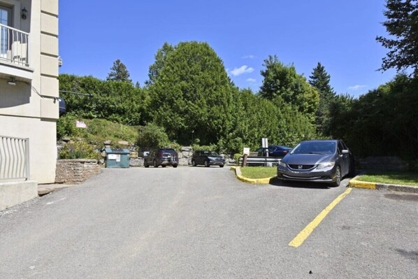 Un estacionamiento con autos, un edificio a la izquierda y árboles al fondo.