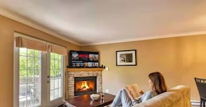A living room with a fireplace, a television mounted above it, and a person reading a book.