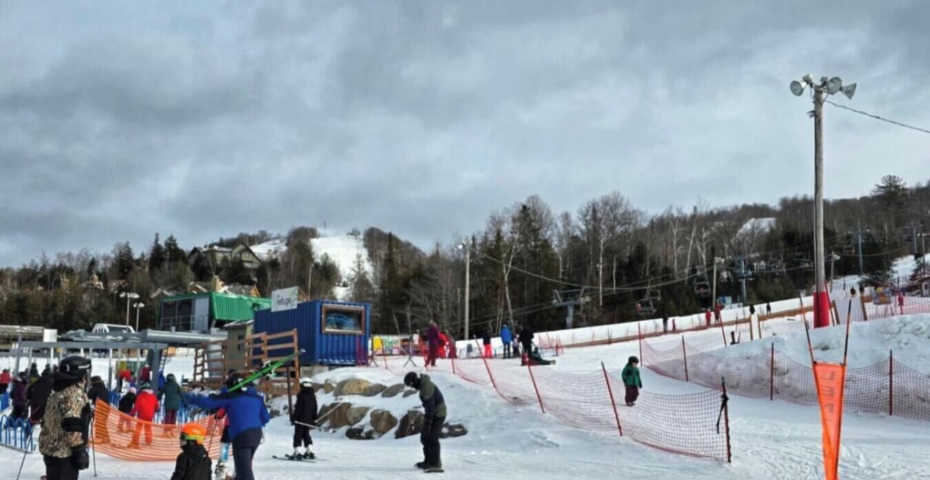 Eine Skipiste mit einem blauen Gebäude, schneebedecktem Boden und bewölktem Himmel.