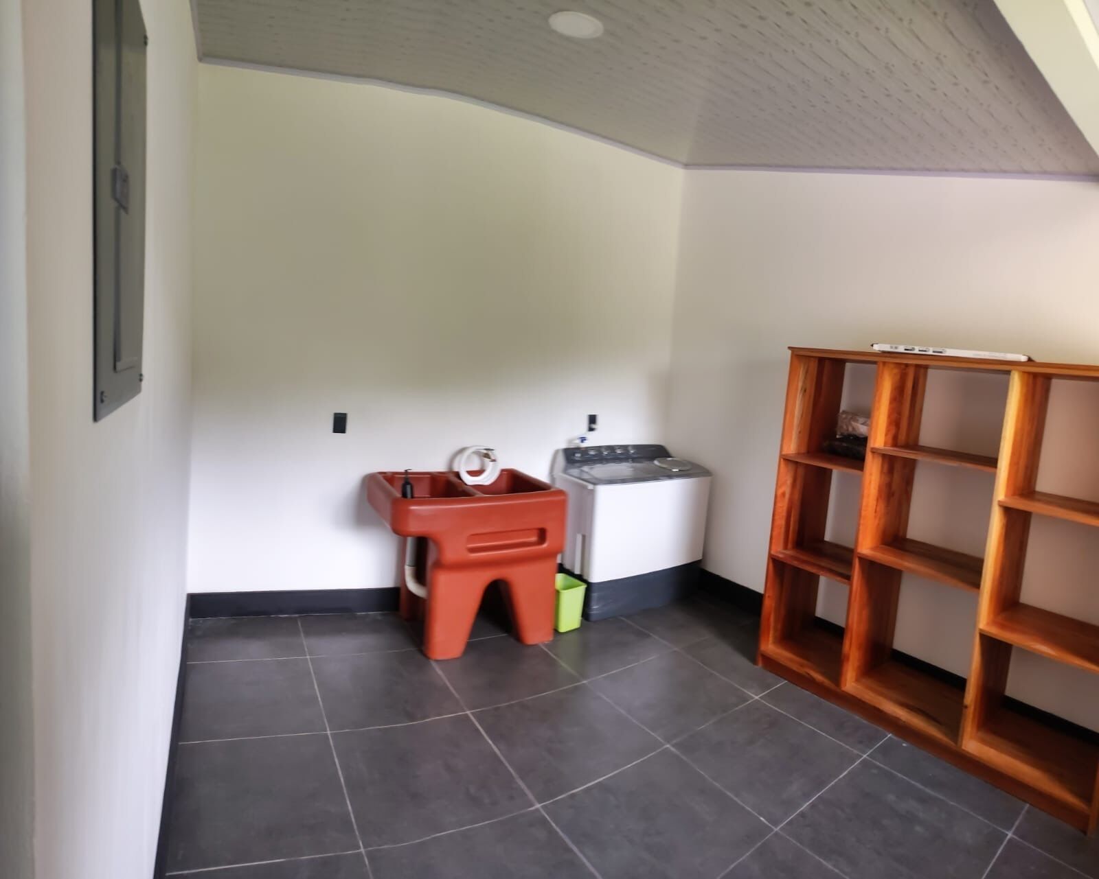 A room with a washing machine, a wooden shelf unit, and a tiled floor.