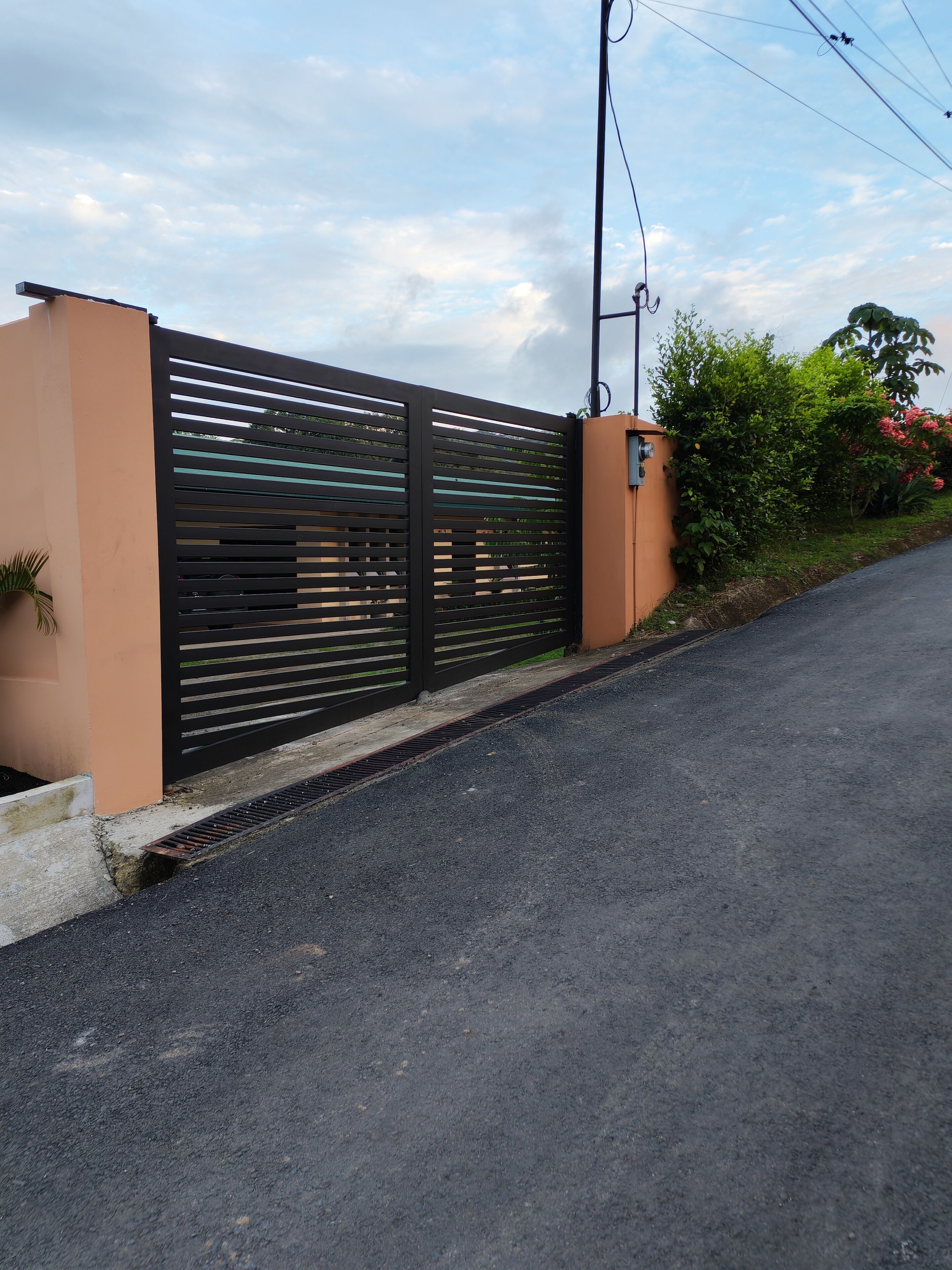 A gated entrance with a metal gate, a concrete pathway, and a road beside it.