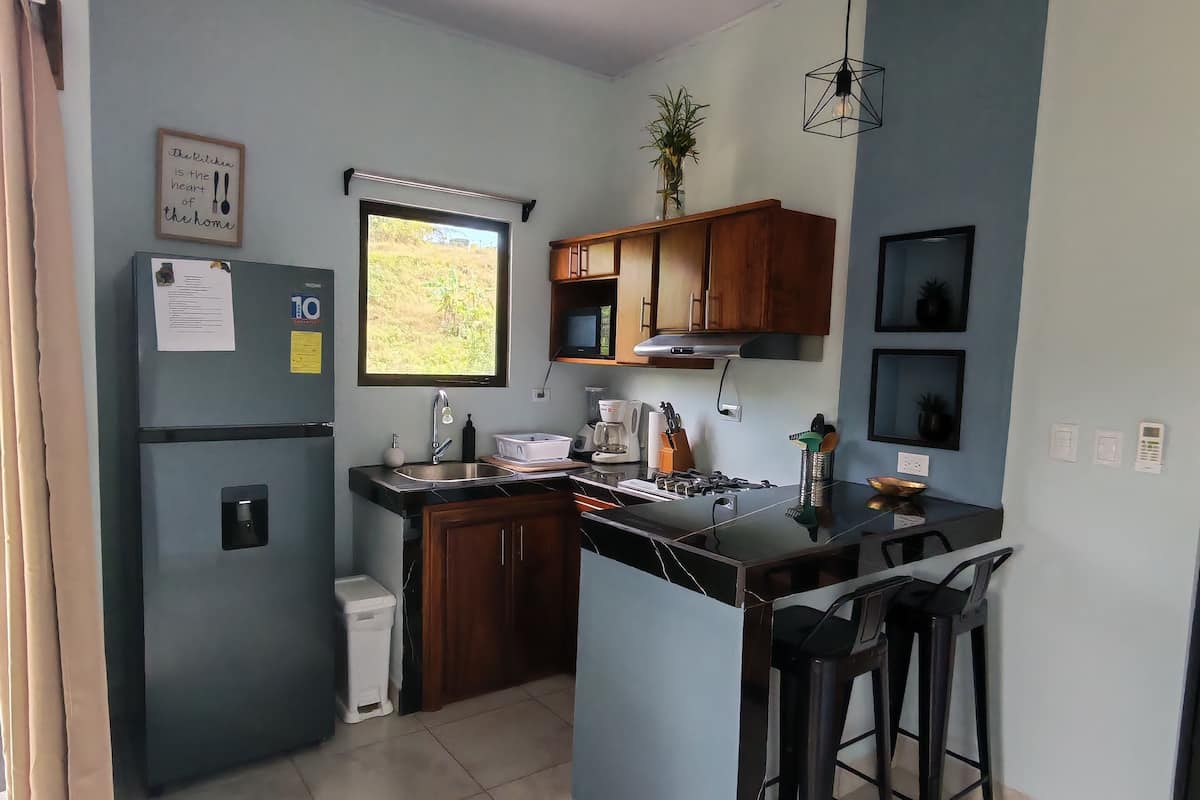 Een kleine keuken met een koelkast, gootsteen en barkrukken.