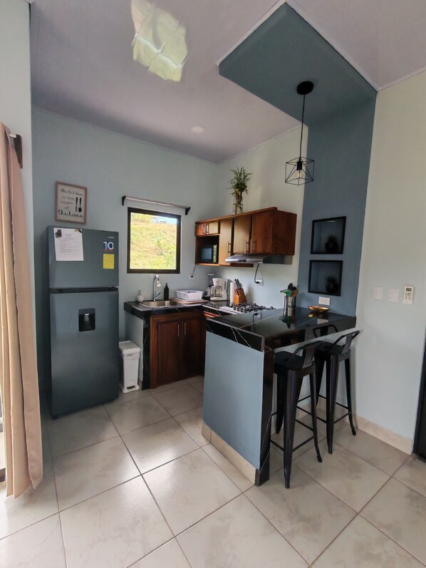 Una cocina compacta con refrigerador, lavamanos y taburetes de bar.