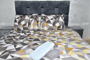 Ein Bett mit einem geometrisch gemusterten Überwurf, zwei Kissen und einem gefalteten Handtuch.