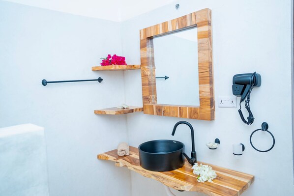 A bathroom with a wooden vanity, a black sink, a mirror, a towel, a hairdryer, and a small shelf with flowers. - CZR Celebrate Zanzibar Rhythm (Jambiani)