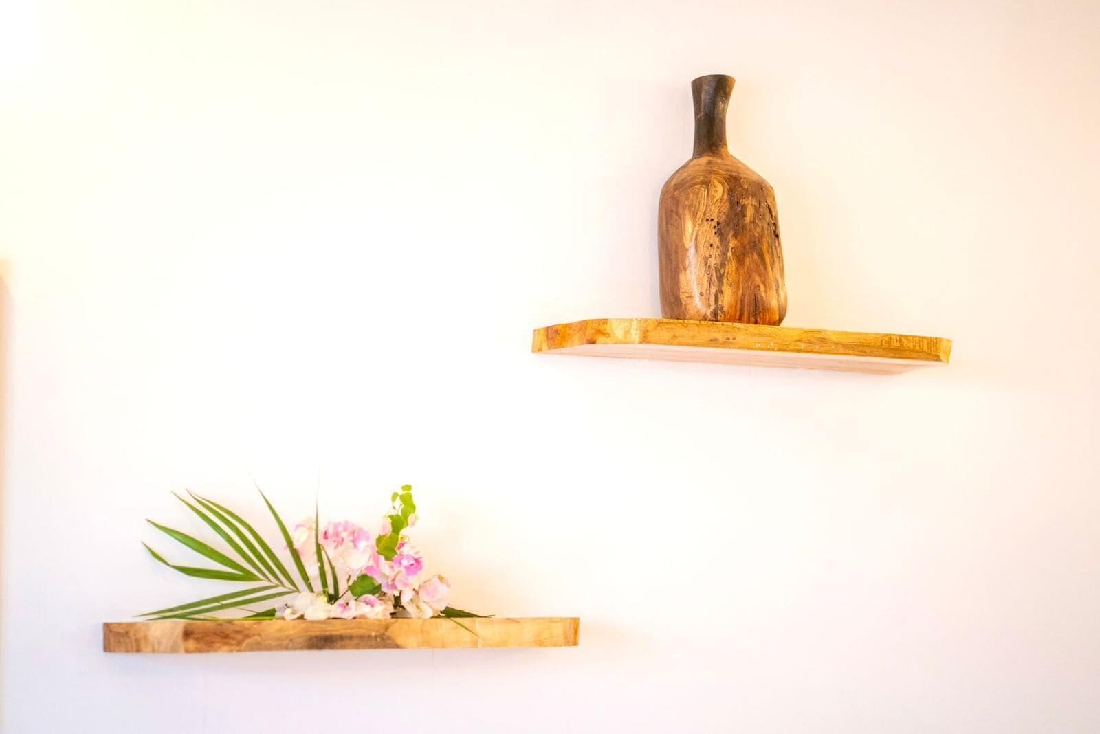 Two wooden shelves, one with a vase and the other with a plant.