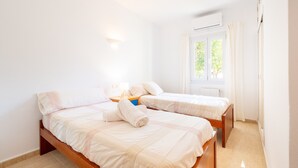 Ein Schlafzimmer mit zwei Betten, einem Fenster mit Vorhängen, einer Wandleuchte und einem Heizkörper.