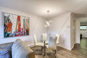 A modern living room with a dining area, featuring a contemporary sofa, a glass table, and a colorful abstract painting.