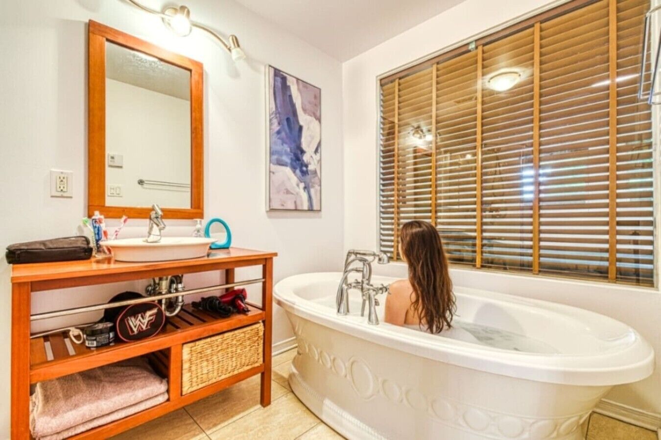 A bathroom with a freestanding bathtub, a vanity with a mirror, and a window with blinds.