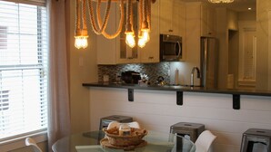 A modern kitchen with a glass dining table, white chairs, and a hanging light fixture. - Waterway Getaway - Myrtle Beach (Myrtle Beach)