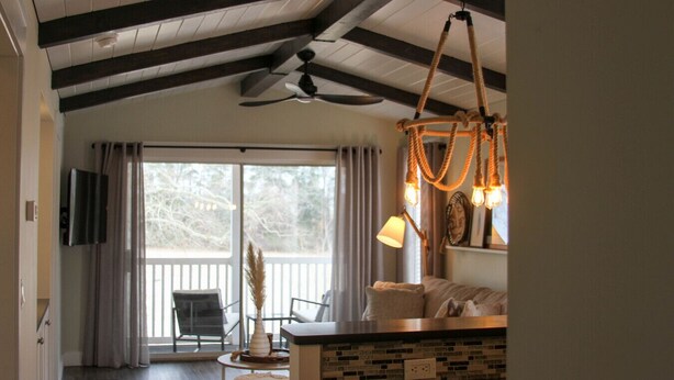 A cozy living room with a ceiling fan, a TV mounted on the wall, a dining area with a table and chairs, and a large window with curtains. - Waterway Getaway - Myrtle Beach (Myrtle Beach)
