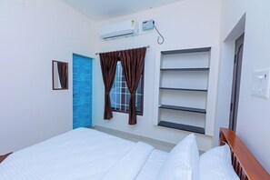 Habitación de hotel con cama, ventana con cortinas, aire acondicionado montado en la pared, una puerta y una estantería.