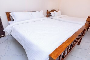 Cama doble con estructura de madera y ropa de cama blanca en una habitación con piso de baldosas.