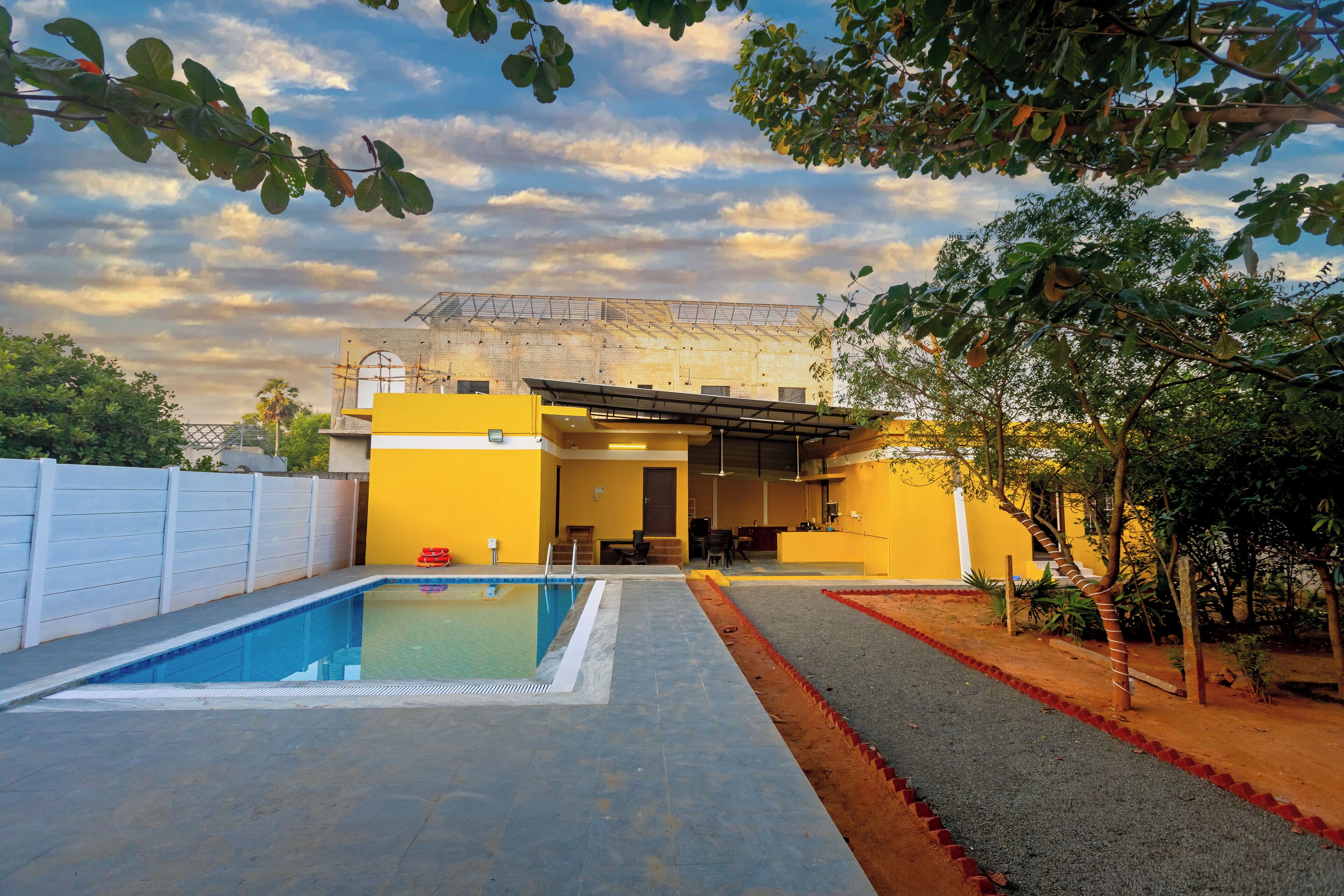 A swimming pool area with a covered outdoor seating area and a building with yellow walls.