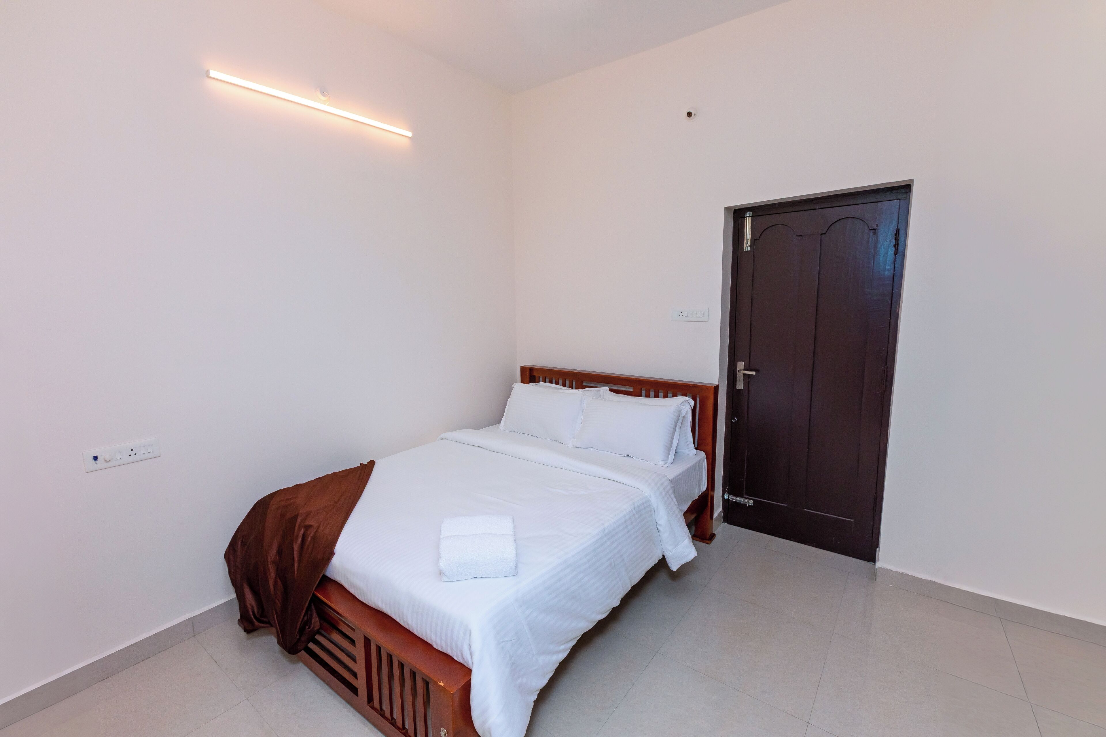 Una habitació d'hotel amb un llit, un panell de fusta al capçal, una porta i una làmpada penjada a la paret.