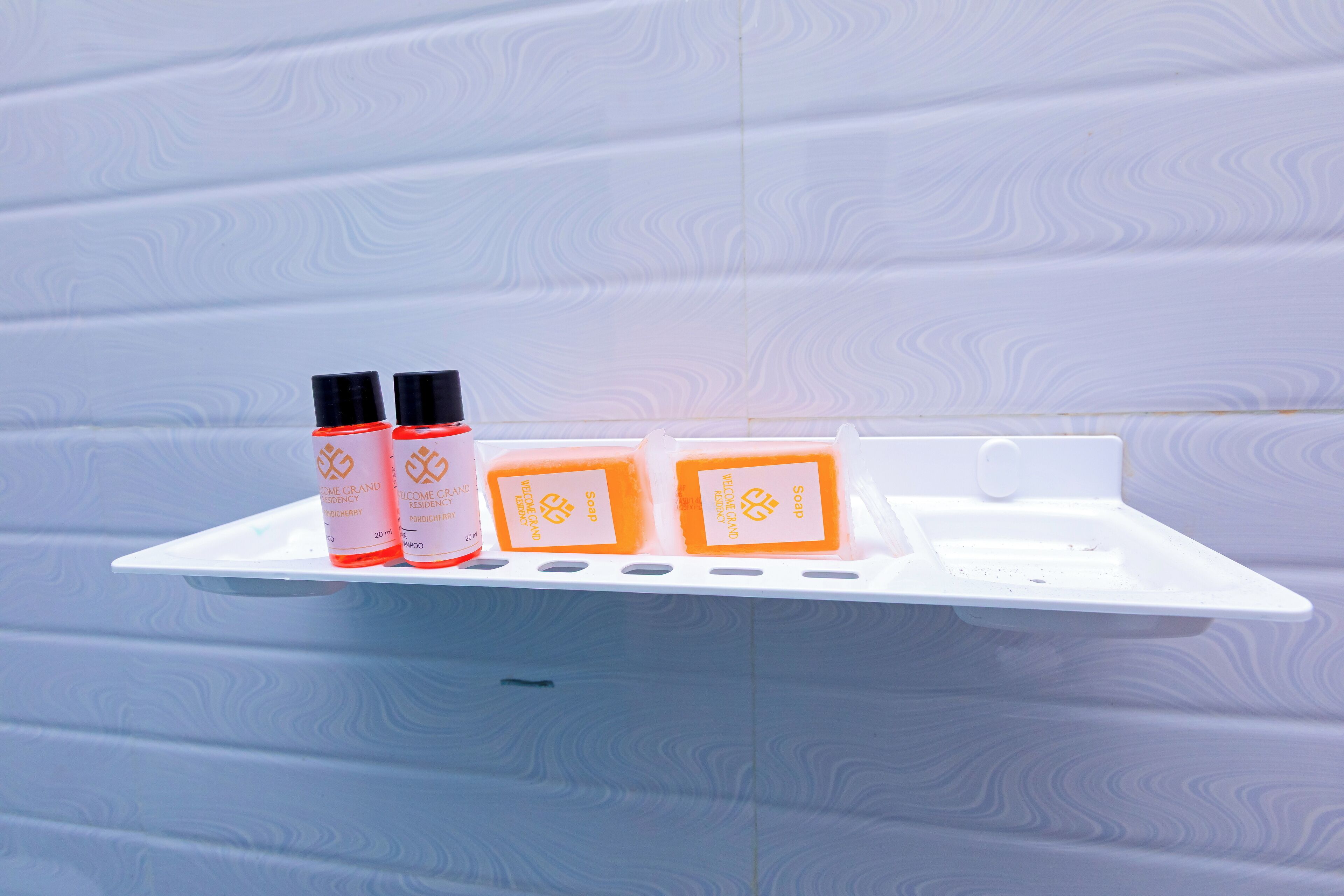 A white shelf with three bottles and two soap bars against a patterned wall.