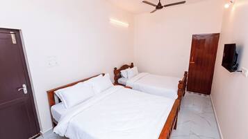 A hotel room with two single beds, a ceiling fan, a TV mounted on the wall, and a wooden door.
