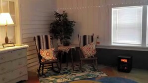 Una habitación acogedora con un aparador blanco, dos sillas con cojines estampados, una mesita, una planta en maceta y una alfombra colorida.