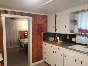 A compact kitchen with wooden cabinets, a dining area with a table and chairs, and a window with curtains.
