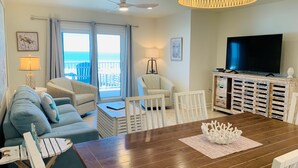 Una sala de estar con una mesa de comedor de madera, dos sofás, un televisor y un balcón con vistas.