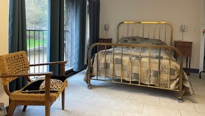 Une pièce comprenant un lit, une chaise, une table de chevet et une fenêtre avec des rideaux.