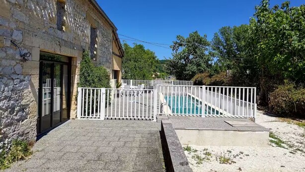 Un bâtiment en pierre doté d’un espace piscine délimité par une clôture blanche.