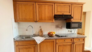 A kitchen with wooden cabinets, a stainless steel sink, a microwave, and a fruit bowl on the countertop. - Suite Seensucht am malerischen Brombachsee (Spalt)