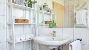 A bathroom with a white sink, shelves with toiletries, a mirror, and a towel rack. - Suite Seensucht am malerischen Brombachsee (Spalt)