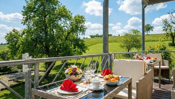 An outdoor dining area with a table set for two, overlooking a grassy landscape with trees. - Suite Seensucht am malerischen Brombachsee (Spalt)