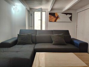 A modern living room with a grey sectional sofa, two patterned cushions, a wooden coffee table, a wall-mounted abstract painting, and a door leading to a bright outdoor area. - Casa della Nonna - One Bedroom House, Sleeps 4 (Castrignano del capo)
