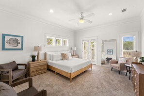 A spacious bedroom with a large bed, a wooden dresser, a chair, and a desk. There are windows with blinds, a ceiling fan, and a door leading to another room. - Coastal 30A Retreat - 4BR - Sleeps 8 - Walk to Beach (Santa Rosa Beach)