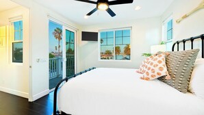 A bedroom with a bed, a ceiling fan, a window with a view of palm trees, and a door leading outside. - Grand 5BD Tri-Level Home with Bay Views Garage Parking AC & Large Patio! (San Diego)