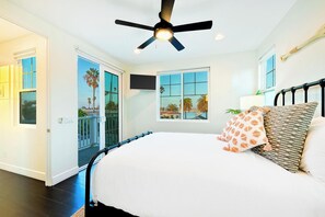 A bedroom with a bed, a ceiling fan, a window with a view of palm trees, and a door leading outside. - Grand 5BD Tri-Level Home with Bay Views Garage Parking AC & Large Patio! (San Diego)