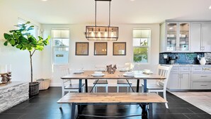 A modern kitchen with a dining area, featuring a wooden table, white chairs, and a large potted plant. - Grand 5BD Tri-Level Home with Bay Views Garage Parking AC & Large Patio! (San Diego)