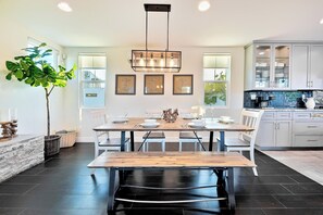 A modern kitchen with a dining area, featuring a wooden table, white chairs, and a large potted plant. - Grand 5BD Tri-Level Home with Bay Views Garage Parking AC & Large Patio! (San Diego)