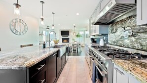A modern kitchen with a central island, stainless steel appliances, and a large stone backsplash. - Grand 5BD Tri-Level Home with Bay Views Garage Parking AC & Large Patio! (San Diego)
