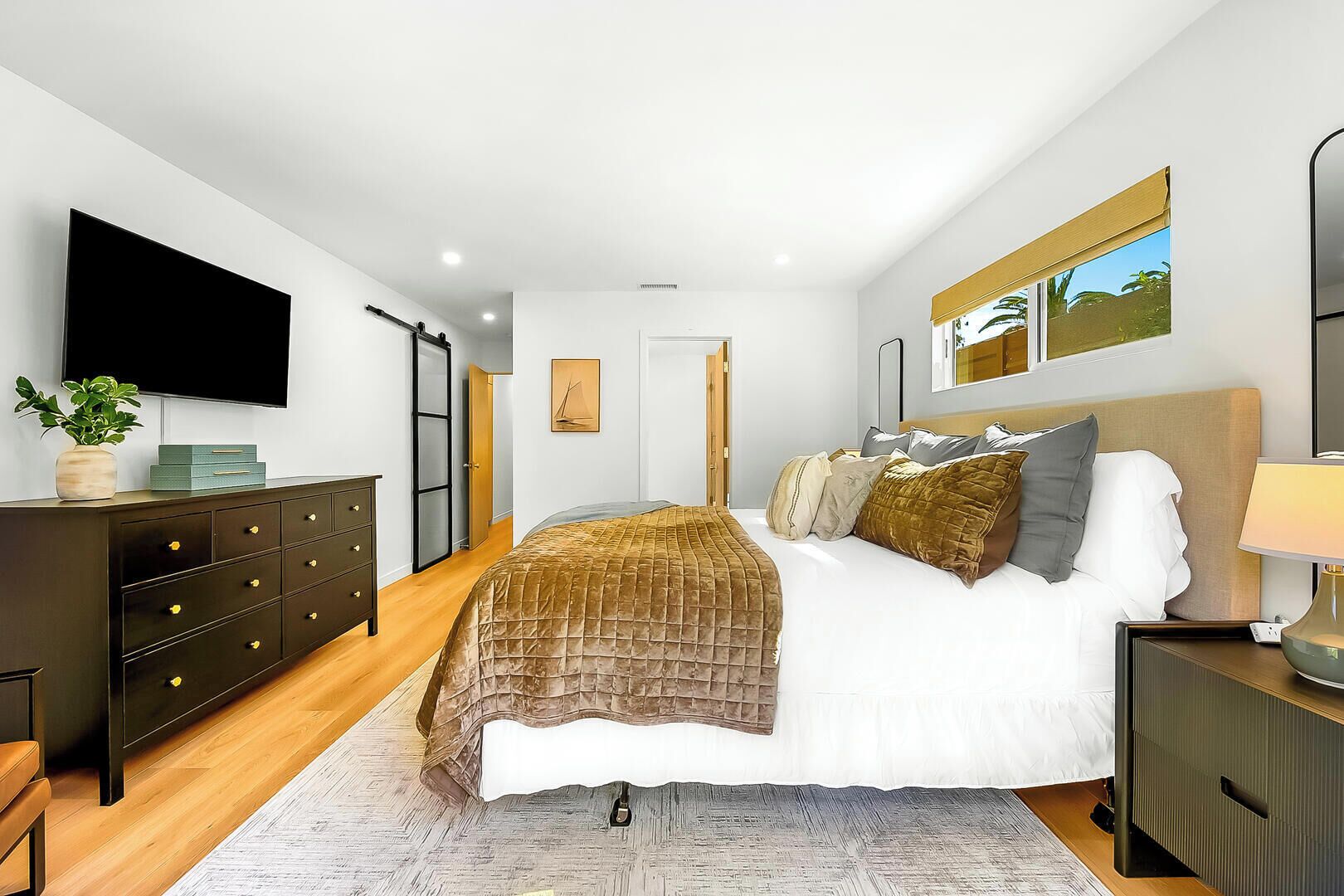 Een moderne slaapkamer met een bed, nachtkastjes, een dressoir, een televisie en een schilderij aan de muur.