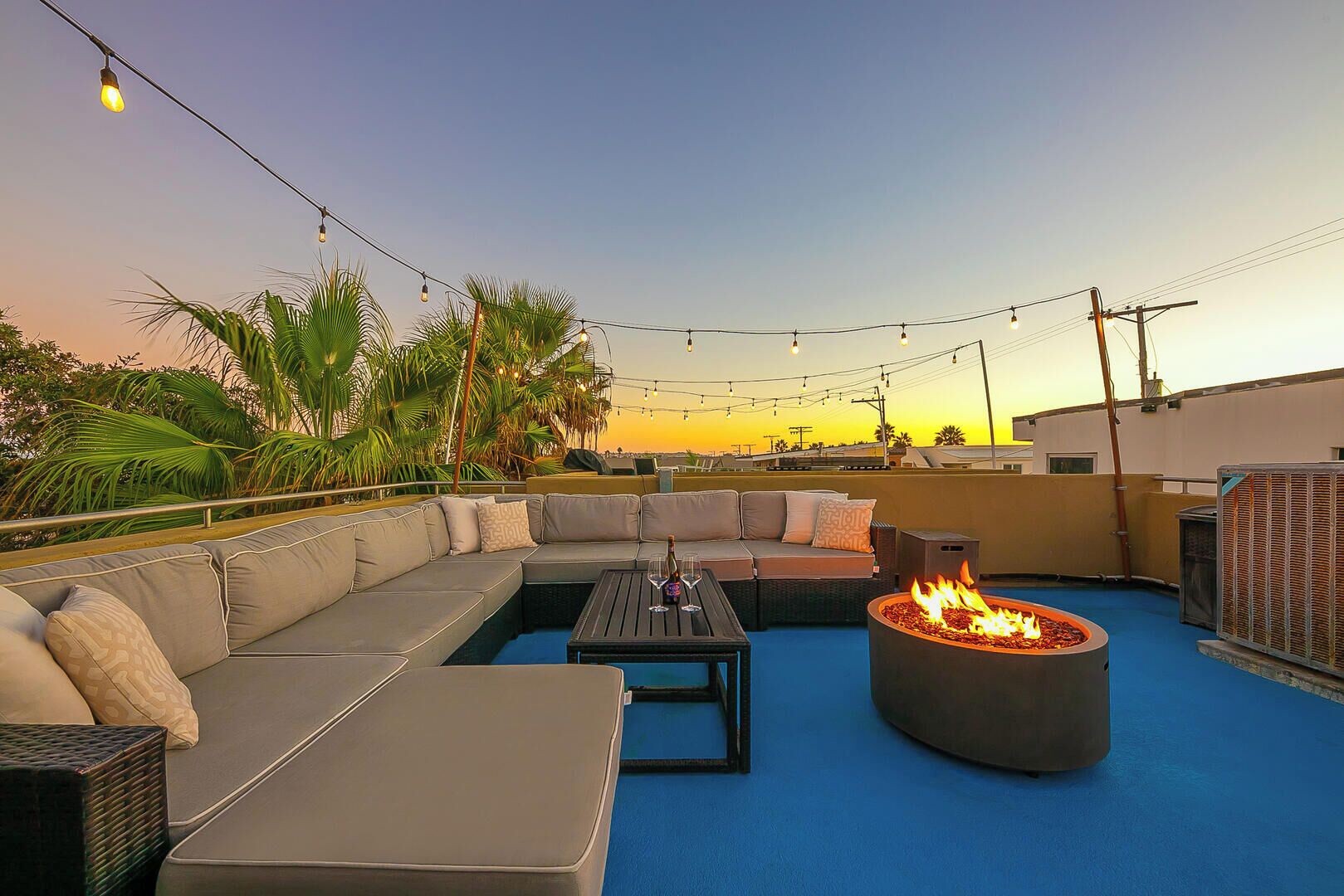 Una terraza en la azotea con un brasero, asientos al aire libre y luces colgantes.