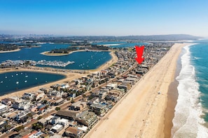 Luftaufnahme einer Küstenstadt mit langem Sandstrand, einer Marina und einem dicht bebauten Stadtgebiet.