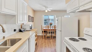 Cocina compacta con armarios blancos, microondas, refrigerador y estufa. Hay una mesa de comedor con sillas y una ventana con vistas.